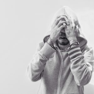 Man in hand cuffs covering his face